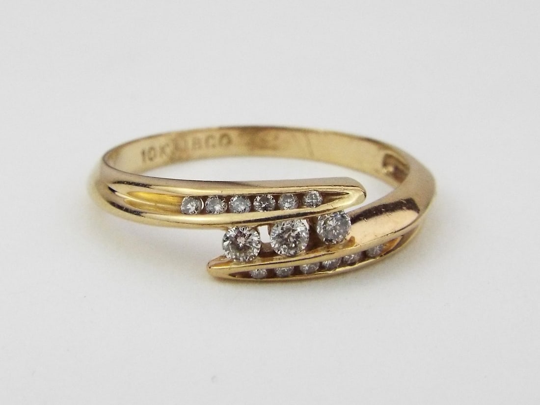BYPASS RING 10K Yellow Gold: Cast 10K yellow gold bypass shank exhibiting minor surface abrasions and light pocket wear consistent with use. Three central round brilliant cut diamonds weighing approximately 0.20 carats total, fla