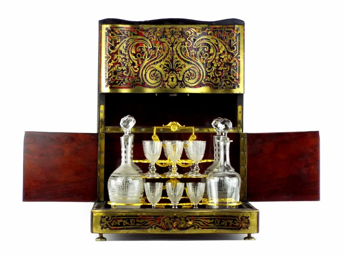 French Napoleonic CAVE A LIQUEUR Boulle Marquetry Bar Set: Beautiful serpentine ebonized body exhibits expected brass lifting and minor veneer loss to the lid and lower plinth. Gilt bronze servante remains solid, holding etched Greek key decanters with facete