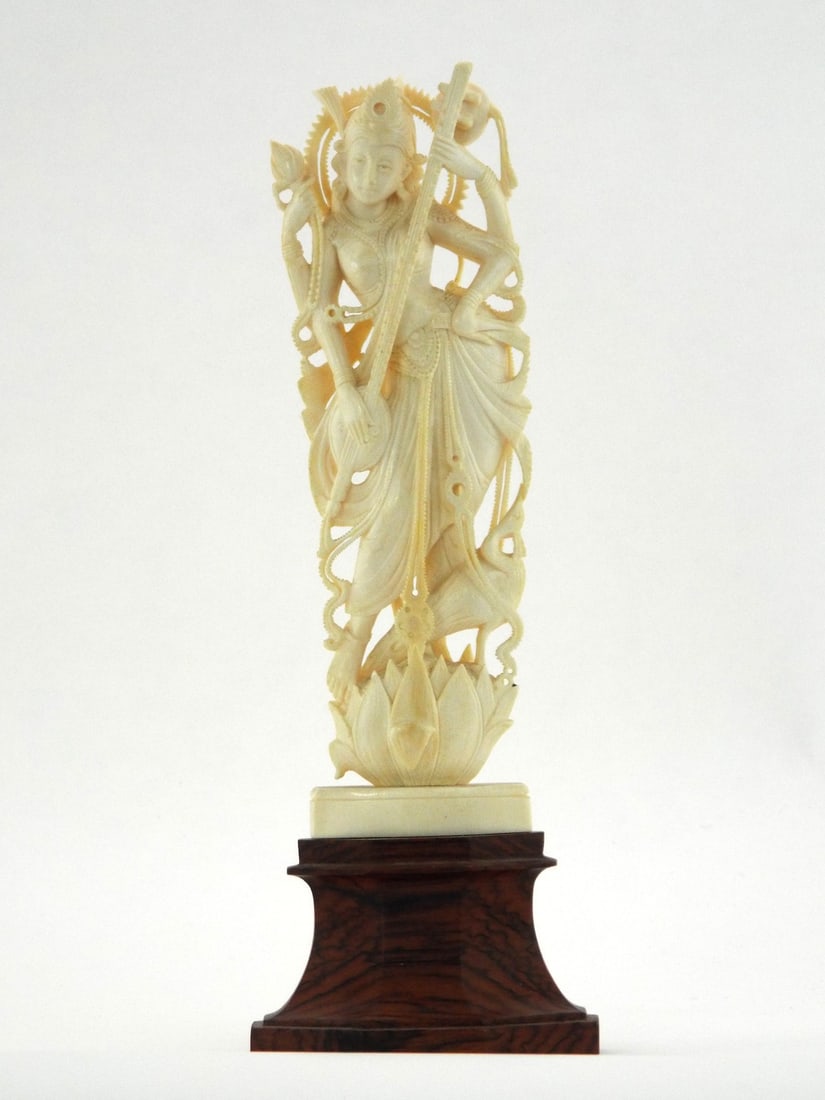 Very Fine Indian CARVED SARASWATI GODDESS with Rosewood Base: Expertly carved monolithic statuette depicting a four armed deity in traditional pose standing upon a lotus pedestal. Body shows fine cross hatching and Schreger lines with minimal yellowing. Intricat