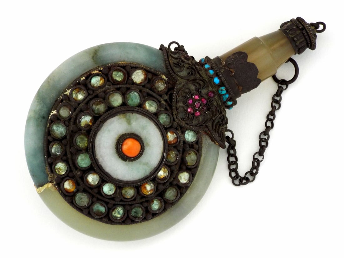 Tibetan 18th-19th C. Snuff Bottle JADE & FILIGREE GEMSTONES: Flattened circular jade body exhibits light green hues with a visible repaired fracture at the base. Ornate silver filigree panels house concentric rings of multicolored glass and stone cabochons with
