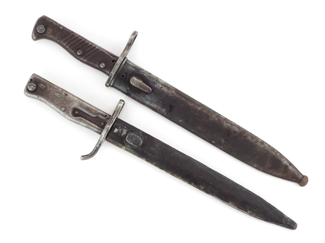 Two German Ersatz Bayonets: Single edged fullered blades showing dark oxidation, runner wear and surface aging. One bayonet features an all steel pressed hilt with a downturned quillon and muzzle ring stamped 2028, the other fea