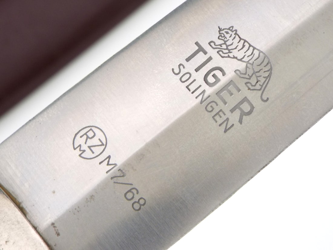 German WWII SA Dagger By Tiger Solingen with RZM MARK: Transitional double edged steel dagger blade features etched motto All for Germany alongside walking tiger logo and control code with light surface runner wear. Brown wood grip retains inlaid insignia