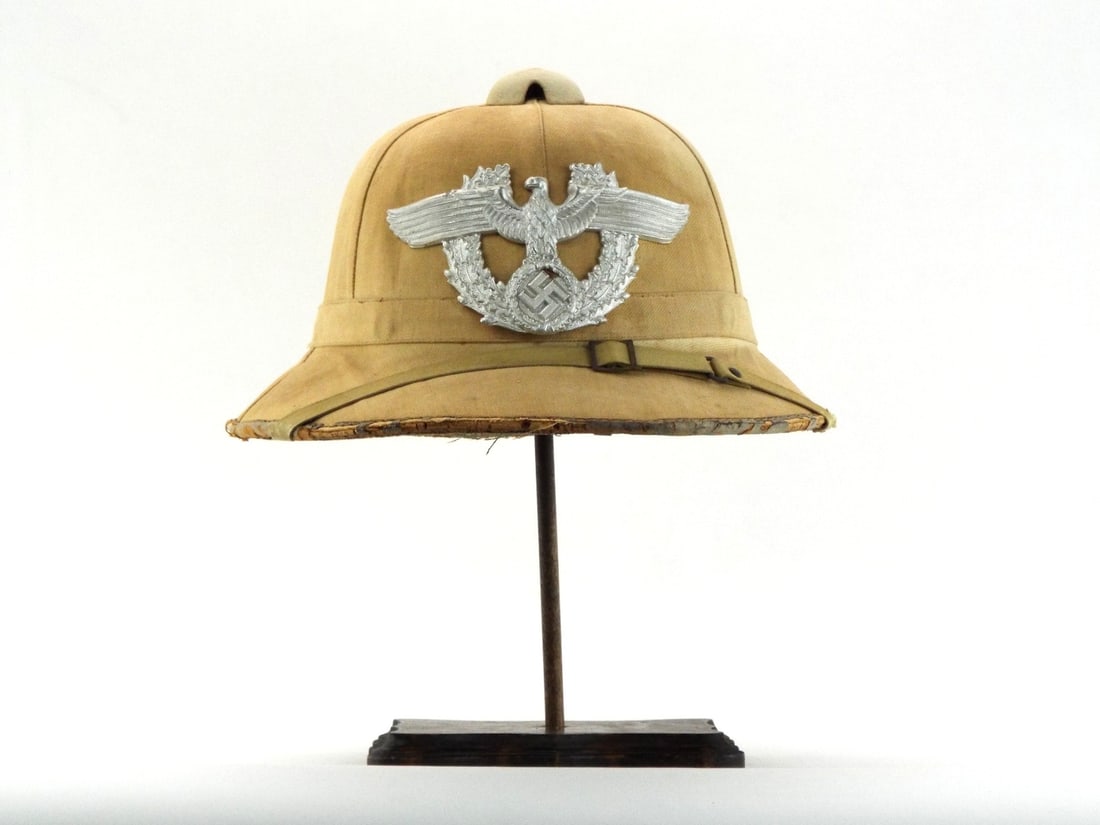 Very Rare German WWII Africa or Mediterranean FIELD POLICE PITH HELMET: Canvas covered cork body exhibits uniform sun fading, moderate fraying and dry rot separation along the leather bound brim edge. The front features a stamped aluminum city protection police badge show