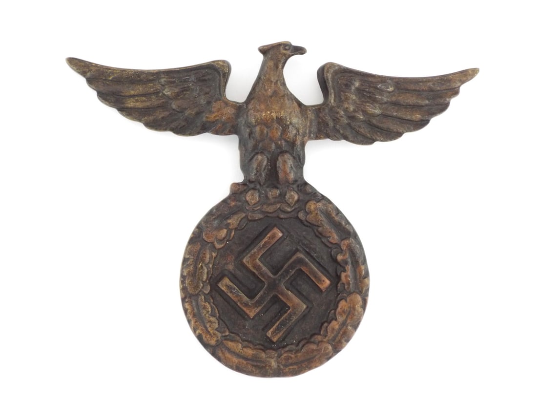 German WWII Political Eagle Plaque Cast Iron: Cast iron political eagle body displaying a dark bronzed patina with light surface wear, featuring a stylized left facing eagle perched upon an integrated oak leaf wreath enclosing a raised ensign.