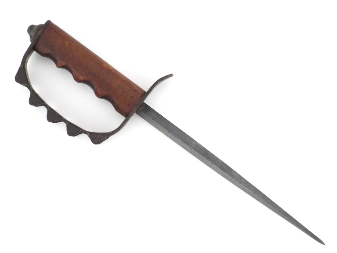 US WWI Trench Knuckle Duster Dagger By AMERICAN CUTLERY COMPANY with Spiked Steel Guard: Features a triangular stiletto blade showing dark uniform patina and minor oxidation over visible blueing. Fitted with a walnut wood grip displaying deep finger grooves and light handling wear, secure