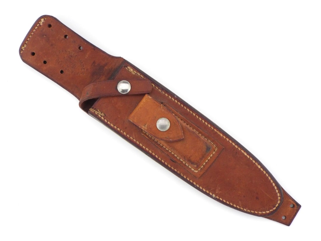 RANDALL MADE KNIVES Sheath: Stout brown leather sheath features heavy contrast stitching, an integral hone pocket with a snap, a diagonal retention strap with snap closure and top/bottom lanyard tie down eyelets. Upper front