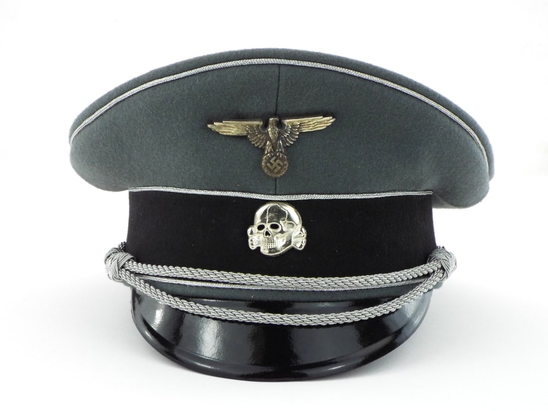 Very Good Quality German Made Post WWII Waffen SS Officer Visor Cap: Field grey wool body displays uniform weave with silver aluminum piping showing minor handling wear and a black velvet band mounting a white metal eagle and death head skull. Silver aluminum chin cord