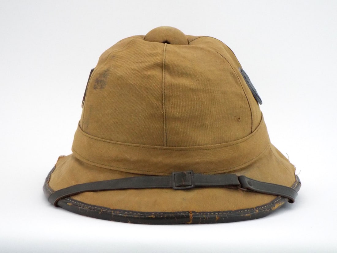 German Post WWII Tropical Pith Helmet Canvas Covered Cork & Dual Metal Insignia Shield: First pattern canvas covered cork body shows moderate field wear, tearing and staining to the twill fabric. Dual prong mounted metal insignia shields retain clear details with moderate oxidation. Chin