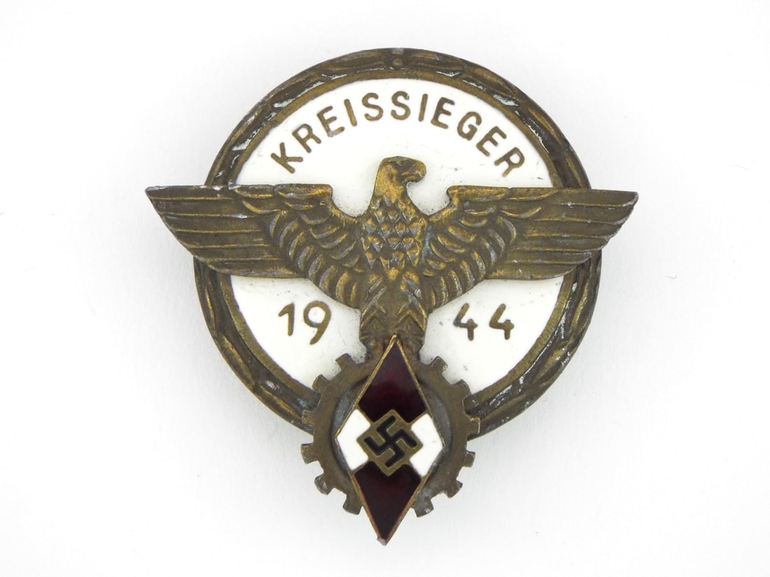 German WWII HJ Vocational District Winner Badge By G. BREHMER with Enameled Inlays: Enameled circular zinc body exhibits minor age tarnishing to the bronze washed finish, showcasing crisp details on the national eagle and lower cogwheel. Central diamond shaped youth organizational em
