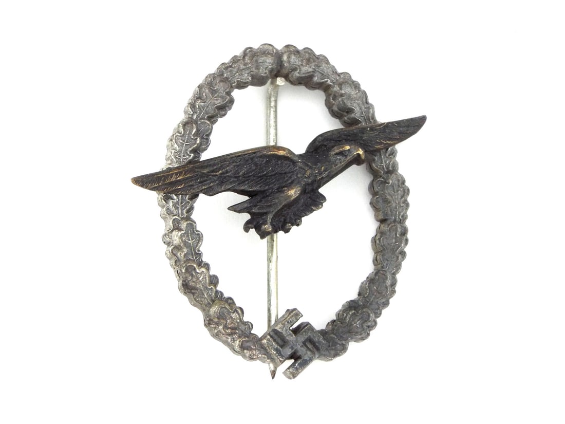 German WWII Glider Pilot Badge By C.E. JUNCKER with Silvered Wreath: Finely struck silvered wreath body with an eagle integrated at the base shows honest wear. A dark oxidized eagle is secured tightly by two reverse rivets. The reverse retains its vertical needle pin, 