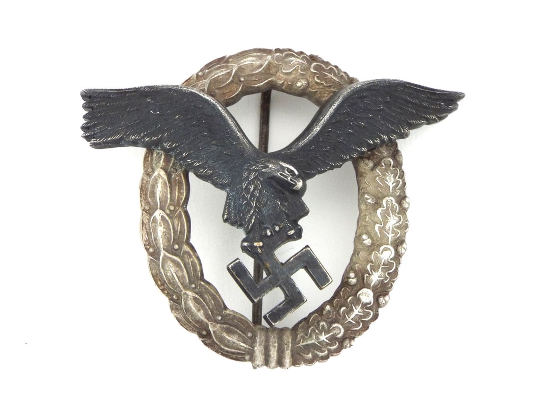 German WWII Luftwaffe Pilot Badge Two Piece Construction: Die struck two piece zinc alloy badge exhibiting a darkened, vaulted eagle riveted to an oval wreath of mixed oak and laurel leaves. Dark grey patination remains strong on the central eagle with minor