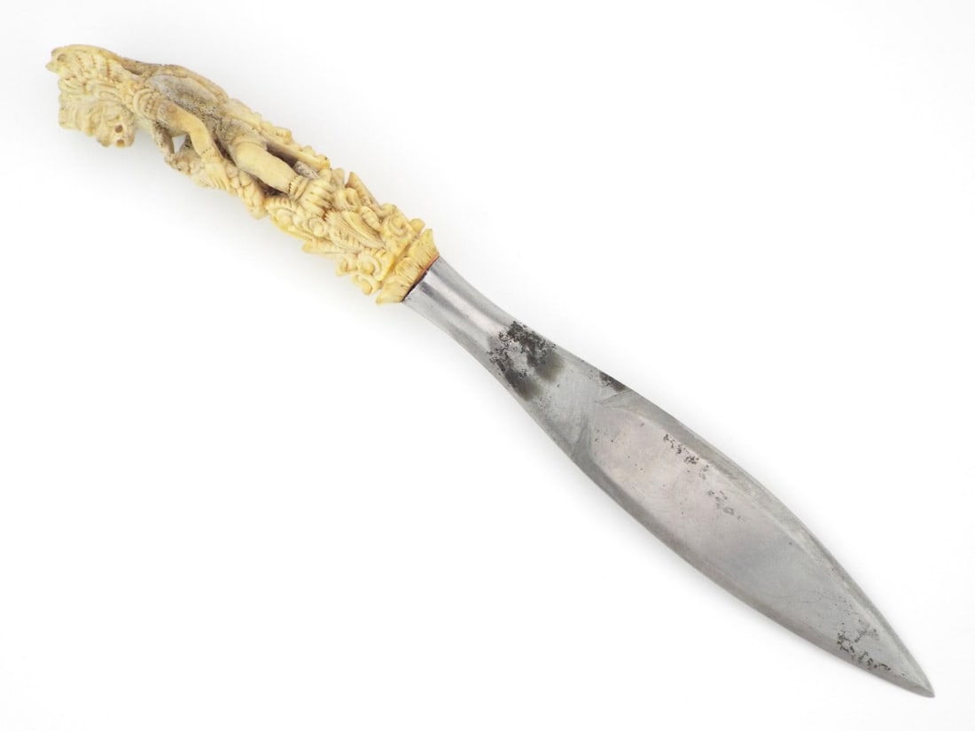 Balinese CEREMONIAL DAGGER Carved Bone Deity Handle: Polished steel spear point blade exhibiting surface abrasions and oxidation consistent with utility. The hilt features a high relief carving of a mythological deity executed in dense bone, showing dee