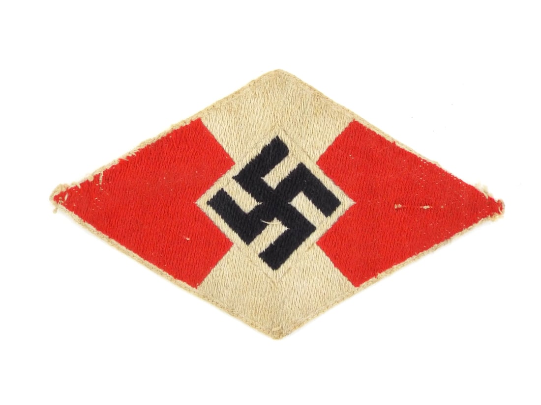 German WWII HJ SLEEVE PATCH Multi piece Construction: Multi piece woven textile insignia featuring a vibrant red and white cotton field arranged in a diamond shaped orientation. The central black ensign is expertly stitched to the white ground, exhibitin