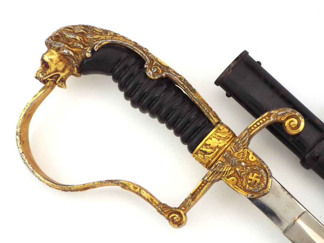 German WWII Army Officer Sword By ALEXANDER COPPEL Gilt Brass Lion Head Hilt: German WWII Officer sword featuring a single edged bright polished steel blade with a maker stamp at the ricasso, showing minor surface scuffs. Brass lion head hilt retains rich gilding with one red s