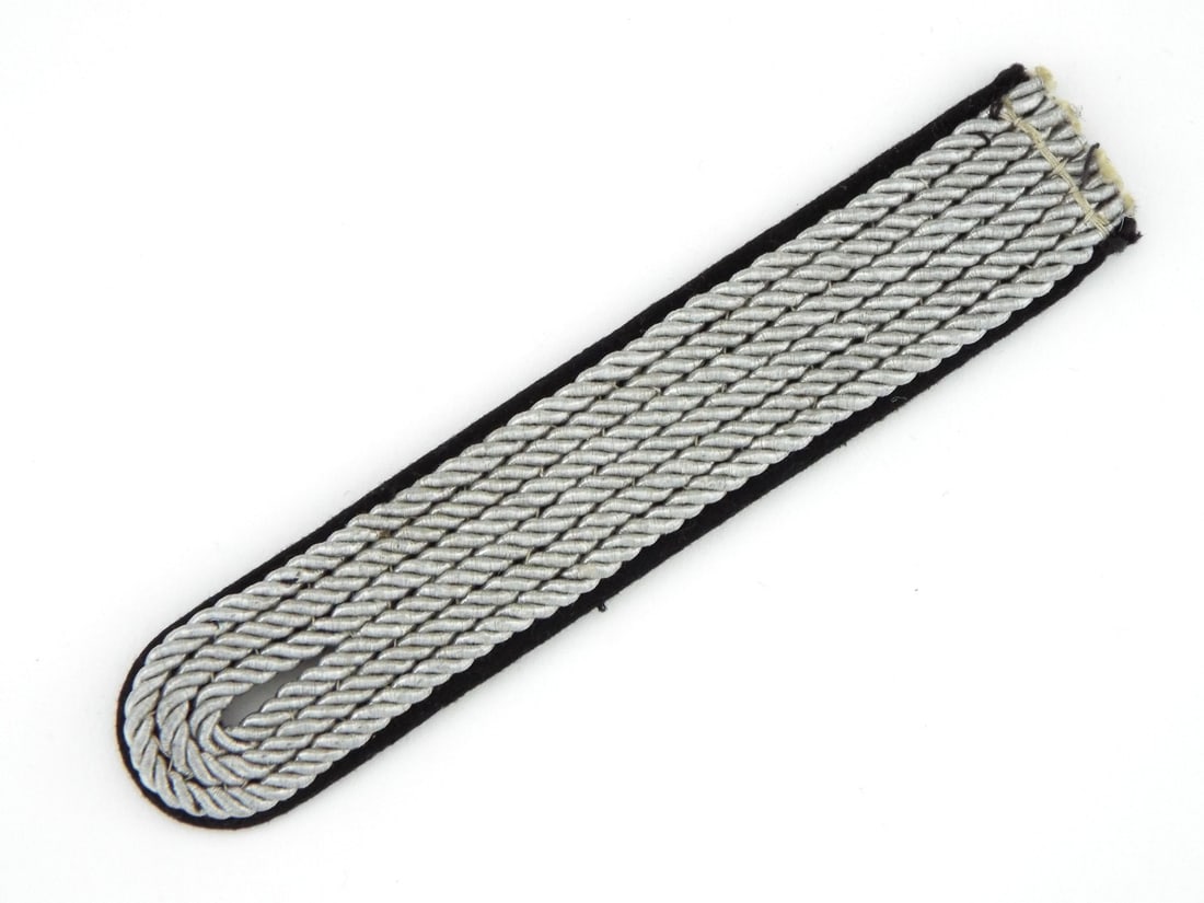 German WWII SS Officer Sew In Shoulder Board with RZM PAPER TAG: Woven bright aluminum cord body retains excellent luster mounted to dense black wool backing cloth. Sew in terminus exhibits minor fraying and untrimmed thread. Backing surface displays light age toni