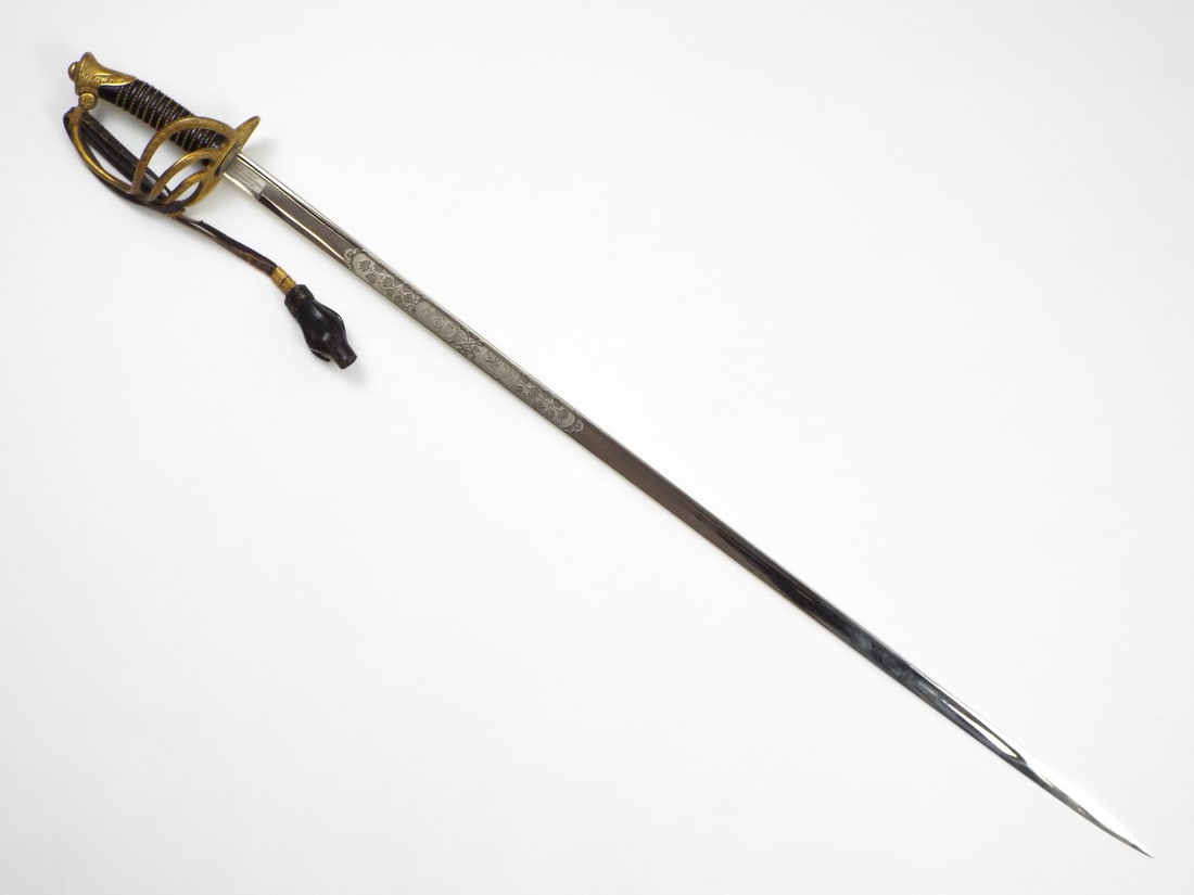 Belgian WWII Infantry Officer Sword By HELDENBERGH VANDEN BROELE & PIGEON with Gilt Leaf Guard: Brightly plated straight blade features engraved foliage, royal lion shield and Leopold III cypher with the motto translated as For the King and the Fatherland. Ribbed black horn grip is tight with wi