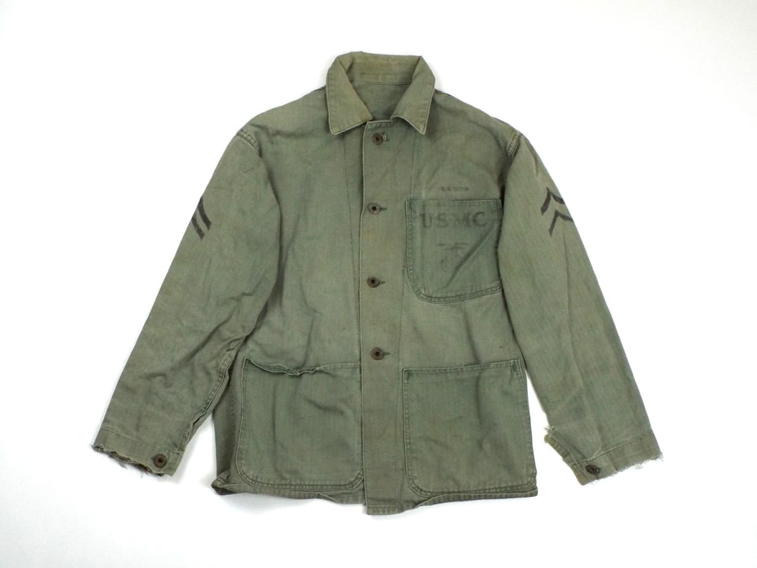 US WWII MARINE CORPS HBT Utility Jacket with Stenciled Chevron: USMC utility jacket crafted from sage olive drab herringbone twill cotton, featuring a three pocket layout with an un flapped left chest pocket bearing an ink stenciled USMC EGA emblem and two un flap