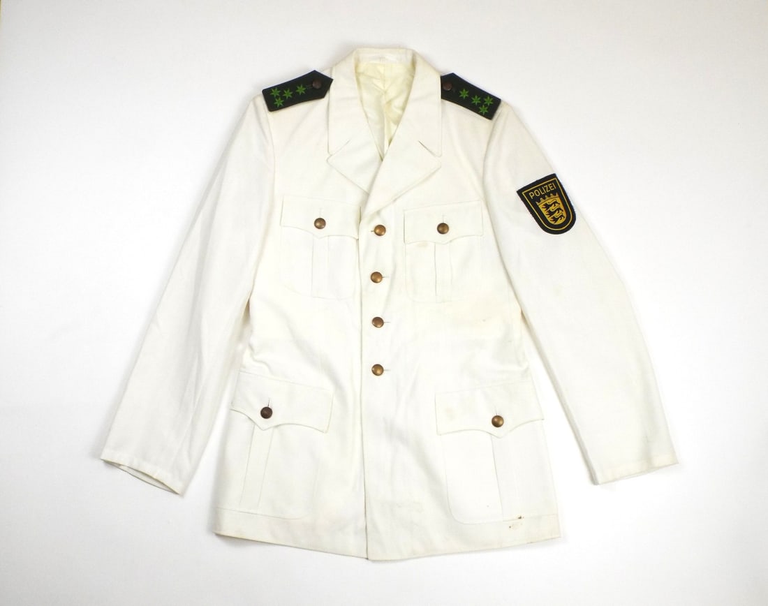 West German Cold War Polizei Summer Tunic BADEN-WURTTEMBERG PATCH: Off white polyester and viscose blend body shows light age toning and minor storage soil throughout, featuring a single breasted four button front, four pleated patch pockets, and pebble finish bronze