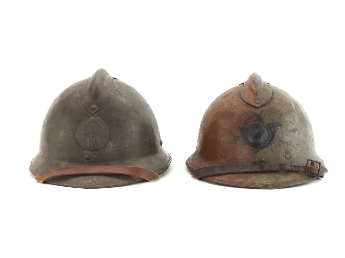 Pair of French WWI M15 Adrian Helmets with HORN & GRENADE Insignia: Pair of Model 1915 steel shells showing age appropriate surface corrosion, scattered paint loss and patination. The first shell retains its dark olive drab finish fitted with a stamped infantry flamin