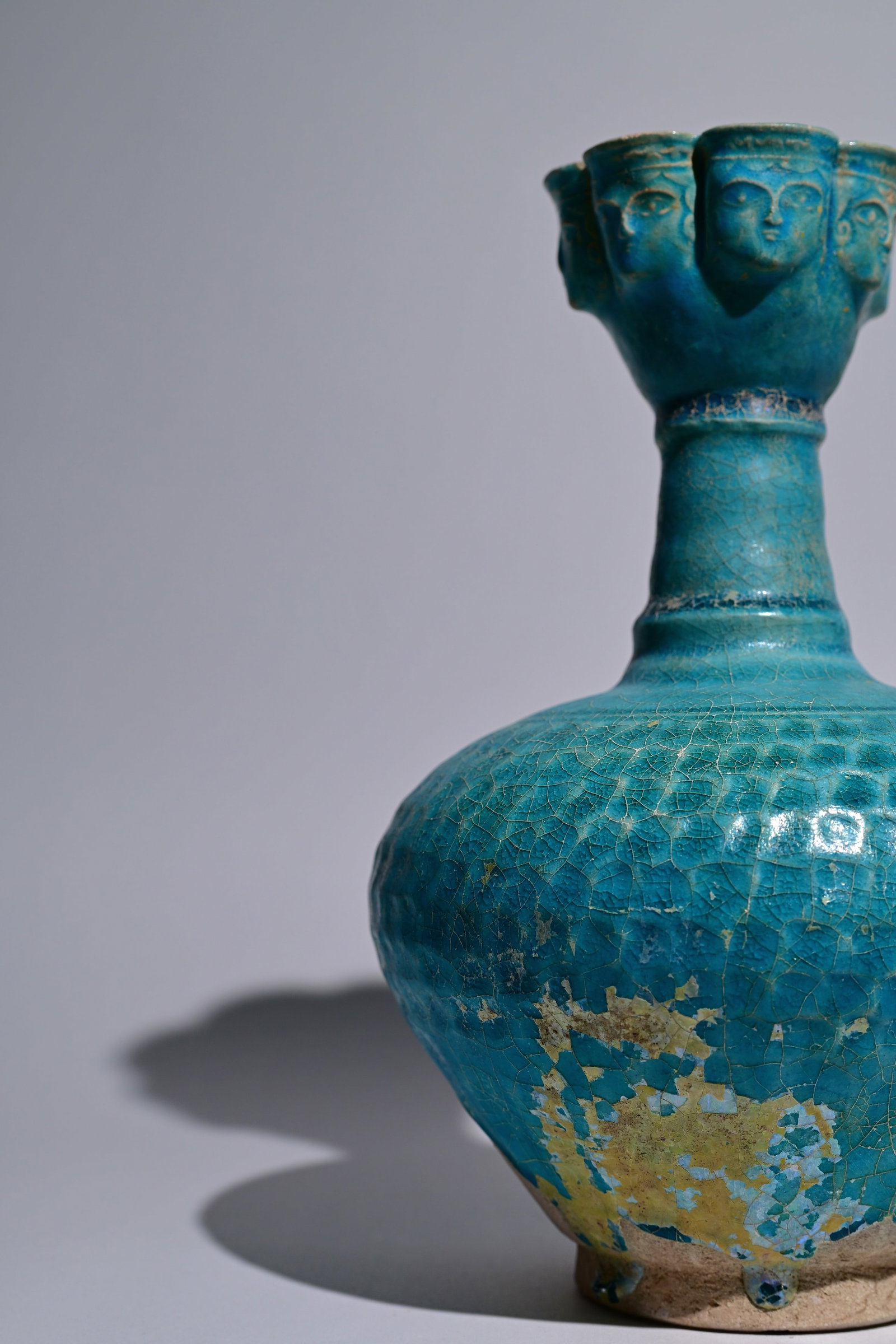 A Nishapur turquoise-glazed pottery bottle, 12th century: A Nishapur turquoise-glazed pottery bottle, North-East Iran, 12th century, with a globular body, tall cylindrical neck, and a distinctive cup-shaped, scalloped mouth. The rim is decorated with seven m