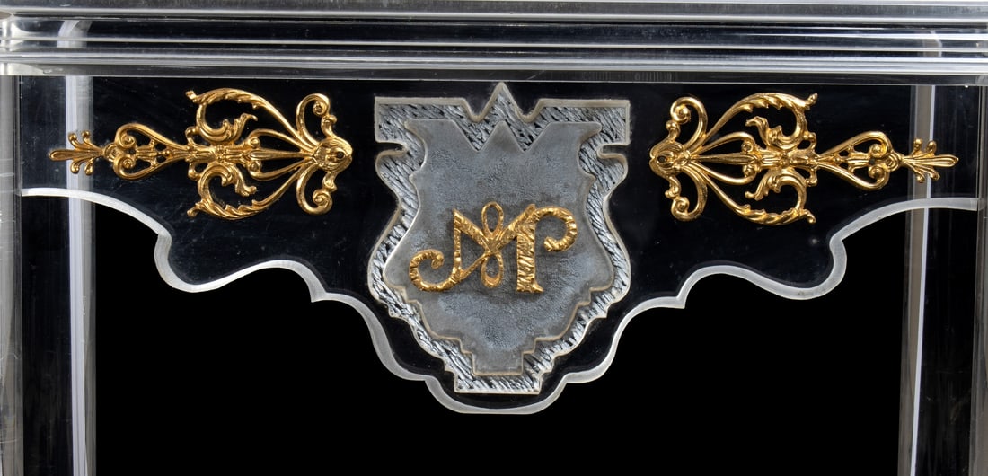 Romeo Tamanti Tavolino in plexiglass trasparente con particolare grambiale sagomato e decoro con: Romeo Tamanti Tavolino in plexiglass trasparente con particolare grambiale sagomato e decoro con monogramma di Max Papiri Piano modanato a tre livelli, gambe cilindriche, grambiale con stemma serigraf