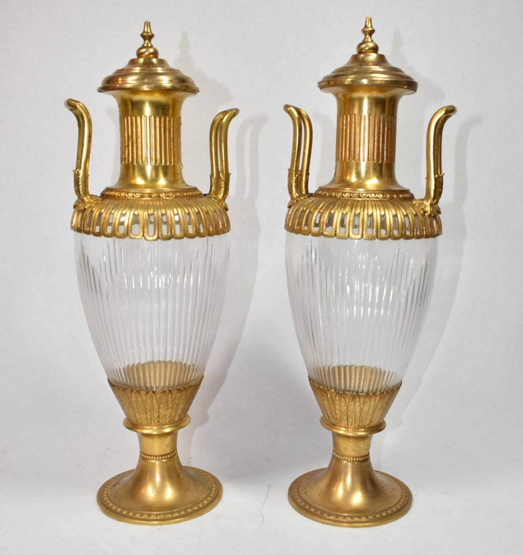 Pair of gilt brass mounted urn form lidded vases: A pair on vintage gilt brass mounted glass neo-classical style urn-form lidded vases. Probably European, early to mid 20th century. Un-marked. Approximate measurements: 16"H x 5" in diameter. Deker Au