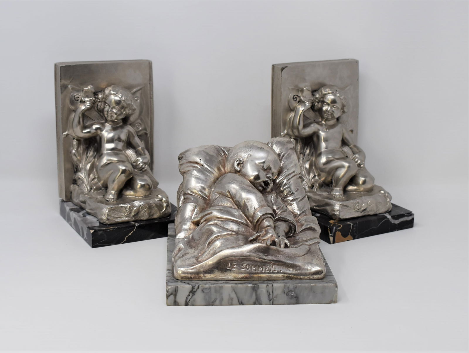 Grouping of antique / vintage bookends: A grouping of antique / vintage bookends including a pair of silver-plated spelter and marble bookends with winged fairies ( 7"H x 5"W x 4.5"D) and a single silver-plated metal bookend featuring a sle