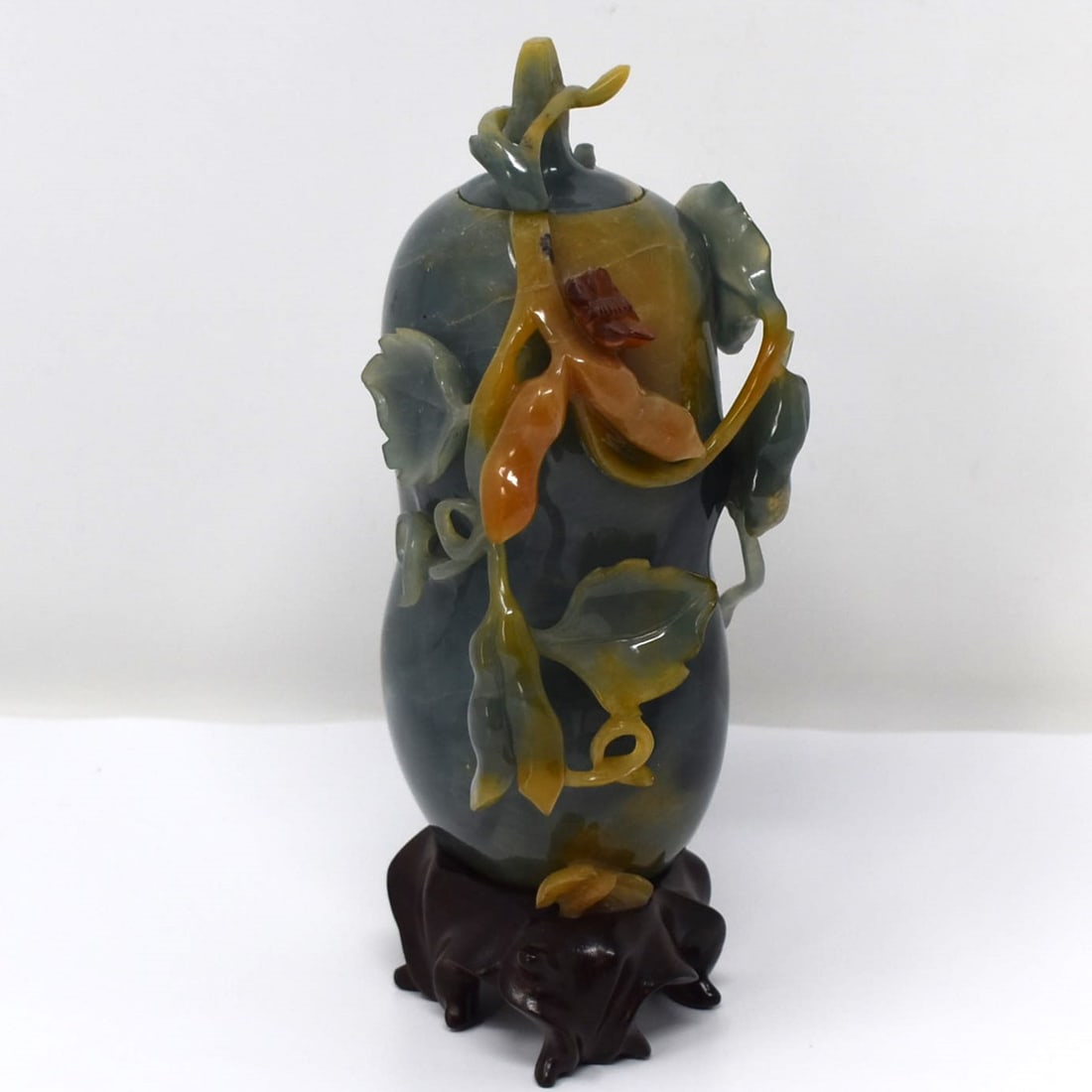 A Chinese carved green jadeite vase and cover: A Chinese carved green jadeite vase and cover on carved wood base. Total height ( including base) 6 1/2"H x 3" in diameter or 16.5cm H x 7.5cm in diameter