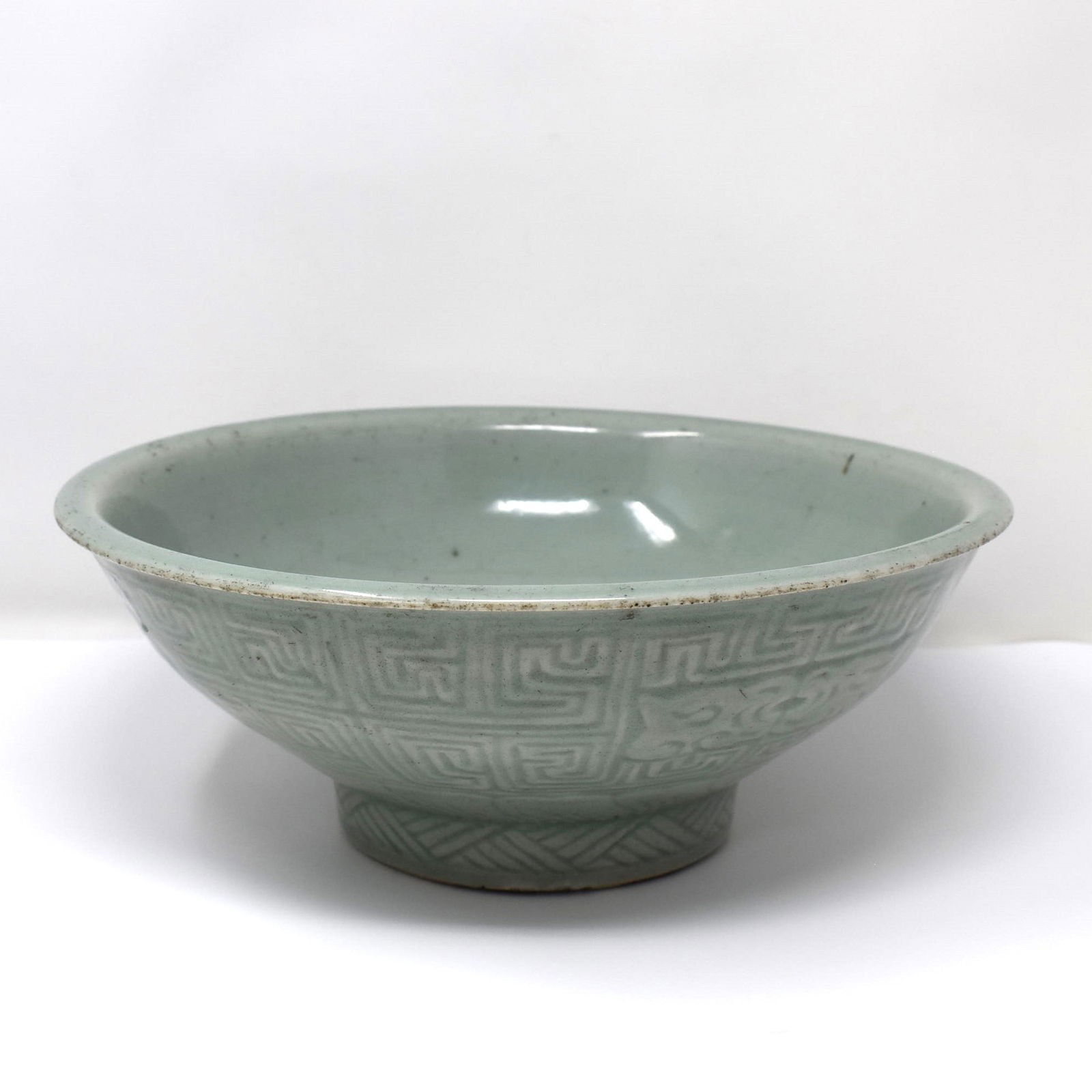 Large Chinese Longquan celadon glazed bowl: A large Chinese carved Longquan celadon glazed bowl, the rounded sides supported on a slightly splayed foot rising to an everted mouthrim, carved around the exterior with geometric motifs below a keyf
