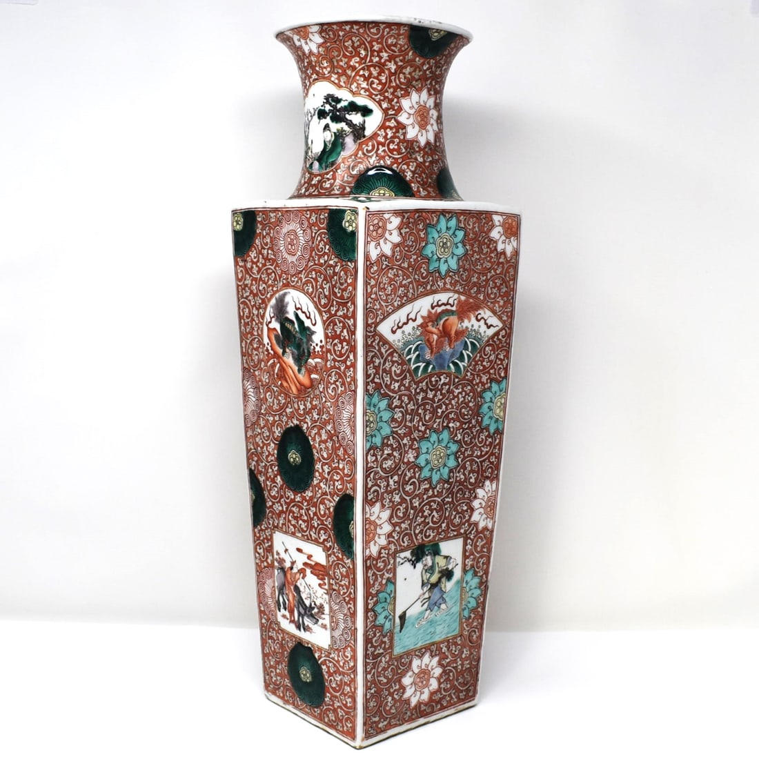 A Chinese famille verte iron-red ground square vase: A Chinese famille verte iron-red ground square-sectioned vase, Qing dynasty. Enamelled to each slightly tapering side with a panel enclosing a qilin above a square figural panel, the neck with a carto