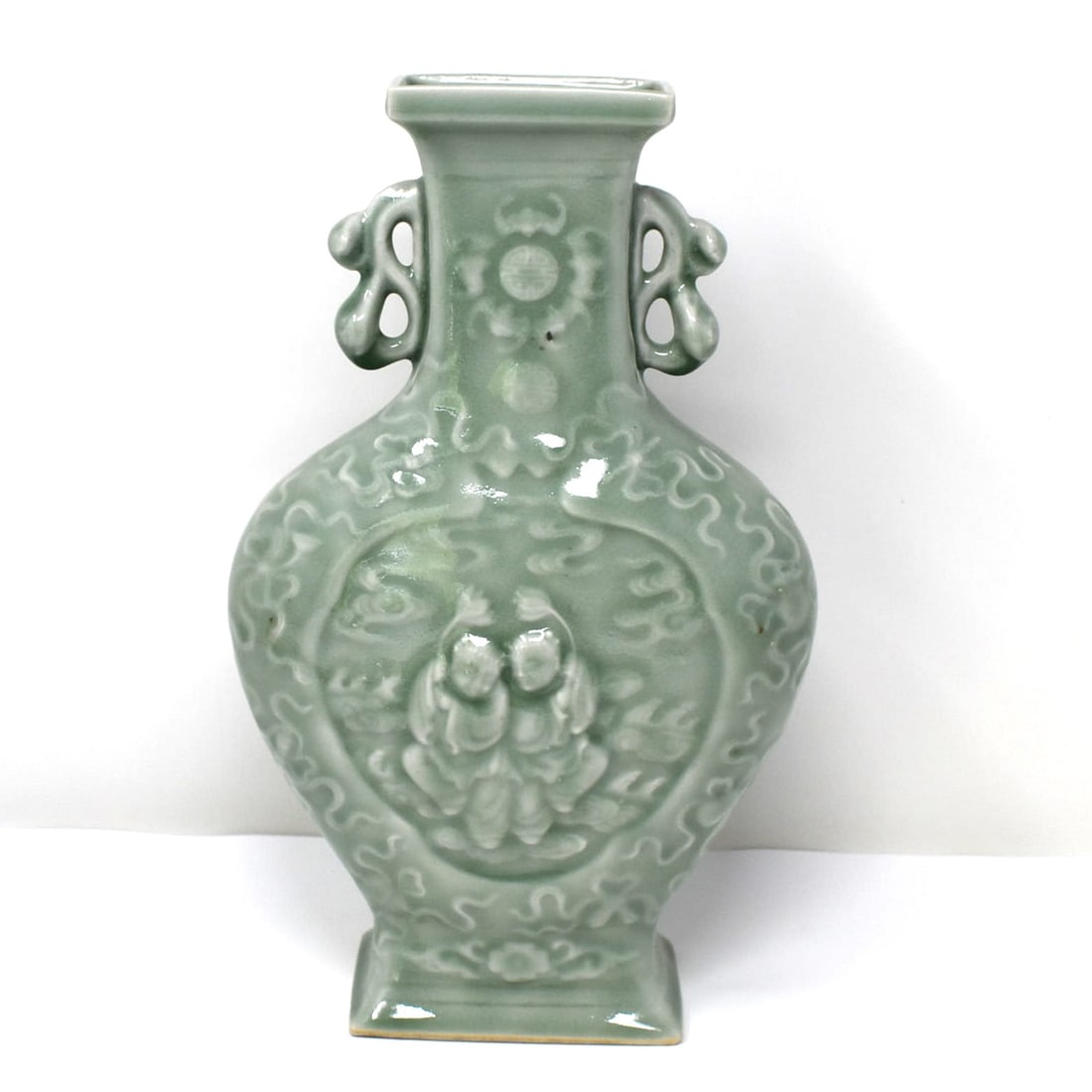 A Chinese carved celadon glazed porcelain vase: A Chinese carved celadon-glazed porcelain vase with central cartouches depicting two children with lotus blossoms. Un-marked. Approximate measurements: 11"H x 6 1/2"W x 3"D or 28 cm H x 16.5cm W x 7.5
