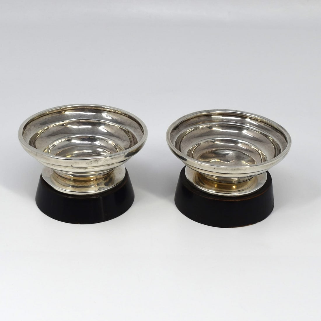 A Pair of English Art Deco sterling silver salt cellars: A Pair of English Art Deco sterling silver salt cellars on custom ebonized wood bases, with Birmingham silver hallmarks for 1936. maker's wak too worn out to be identified. Weight: 2.79 Troy Oz or 87g
