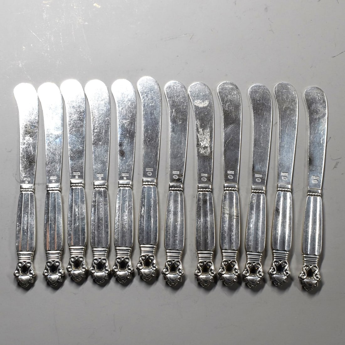 A grouping of 12 GEORG JENSEN 'Acorn' pattern sterling silver butter knifes: A grouping of 12 Georg Jensen 'Acorn' pattern sterling silver butter knifes. Model designed by Johan Rhode in 1915, Denmark. Five of the butter knives with Georg Jensen Sterling silver marks from 1933