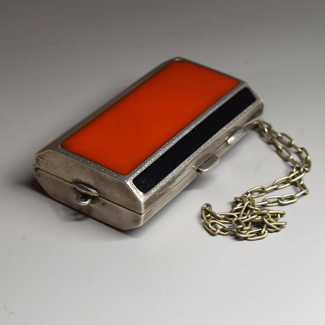An Art Deco silver and enamel barrel-form vanity case with chain: An Art Deco period continental silver and enamel vanity case with chain circa 1925. The hinged case with dual hinged, gold washed interior and mirror, and alternating red and black enamel. Apparently