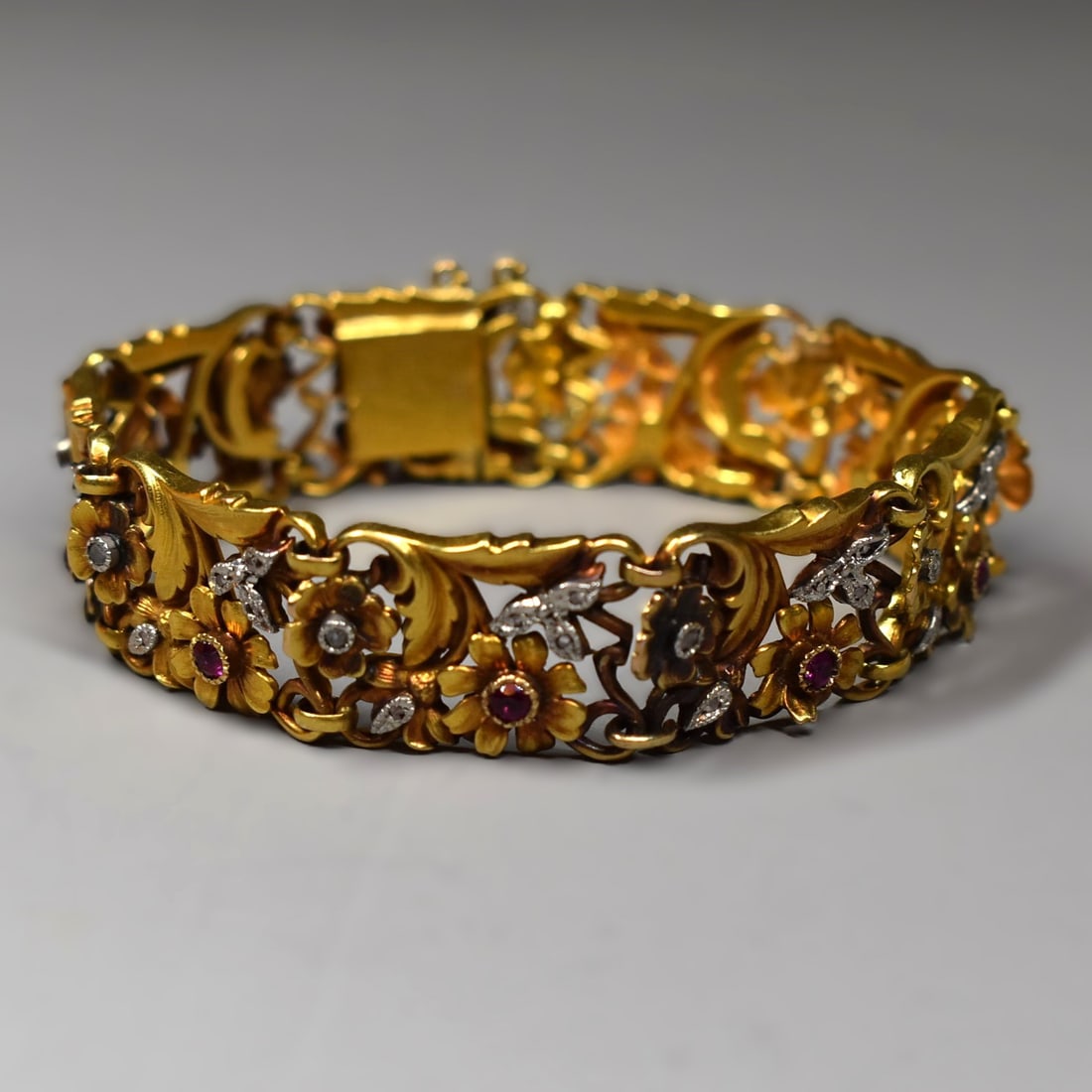 A French Art Nouveau 18K yellow gold bracelt with ruby and diamond accents: An antique French Art Nouveau period (circa 1905) 18K yellow gold articulated bracelet featuring a detailed floral design with ten intricate openwork section-links with diamond and ruby accents. The b