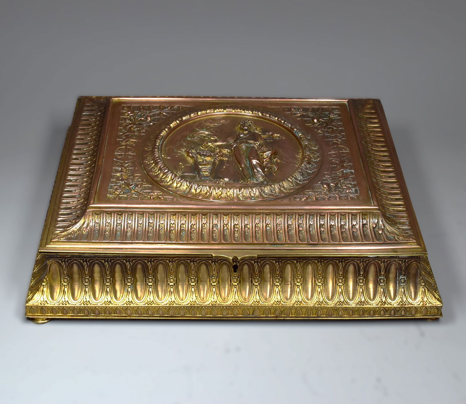 A large antique French gilt brass hinged box circa 1900: A massive antique French gilt brass hinged box circa 1900. Very nicely cast, raised on four feet, the lid with central motif featuring a Greek hiereia, or priestess. Apparently un-marked. Approximate