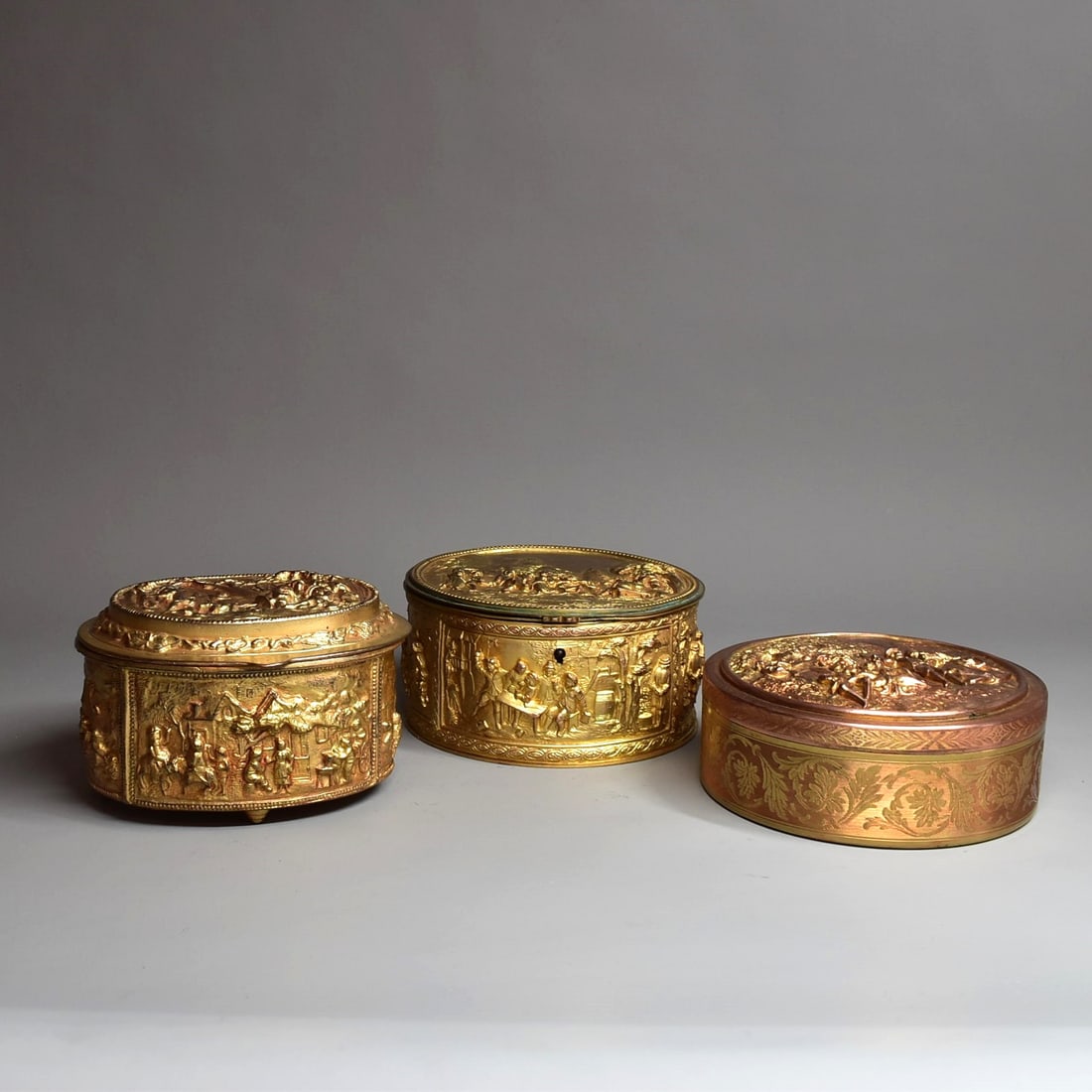 A grouping of three French gilt brass dresser boxes circa 1900: A grouping of three large French gilt brass dresser boxes circa 1900, including two hinged boxes and one box and cover, all three with raised decoration featuring 18th century style outdoor scenes. Ap
