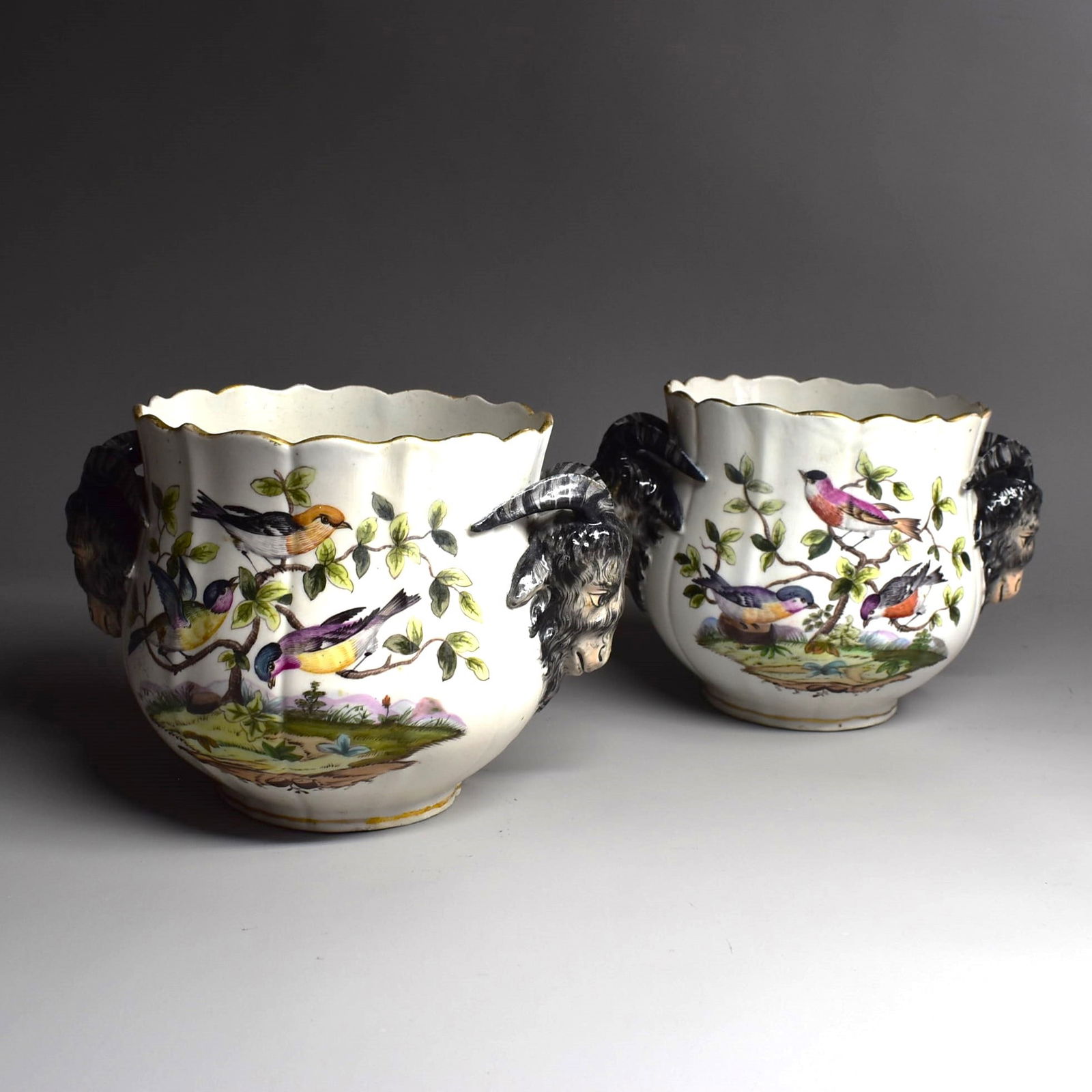 A pair of antique German porcelain cache pots with ram's head handles: A pair of antique German porcelain cache pots with ram's head handles and decoration featuring birds on branches. The undersides with meissen style marks. Approximate measurements: 5"H x 8"W x 6"D or