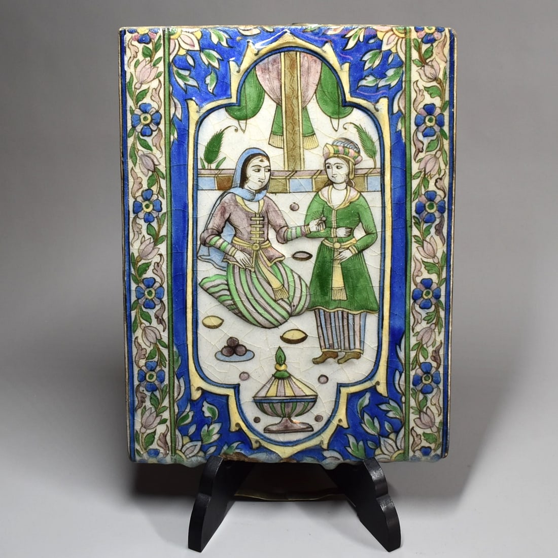 Qajar moulded pottery tile, Persia (Iran), 19TH century: An antique Qajar moulded pottery tile, of rectangular form, decorated under a clear glaze in manganese blue, green, brown, yellow and white, depicting two women in an interior. Persia (Iran), 19TH cen