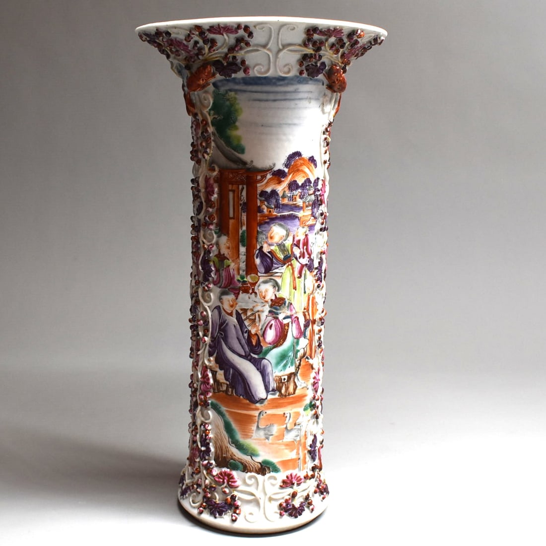 A Chinese export Mandarin palette porcelain famille rose Trumpet vase, Qing Dynasty: An antique Chinese export Mandarin palette Famille rose trumpet vase with beautifully painted court scenes in vignettes on each side and with intricate applied raised grape vine and squirrel motifs on