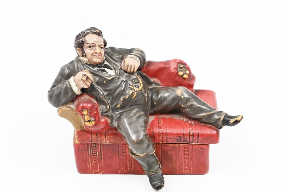 Antisemitic tobacco box (?), Austria, 19th century. A terracotta tobacco box representing a Jew: Antisemitic tobacco box (?), Austria, 19th century.A terracotta tobacco box representing a Jew resting on a chaise longue.Signed VH below base, numbered 80.Size: 11 cm