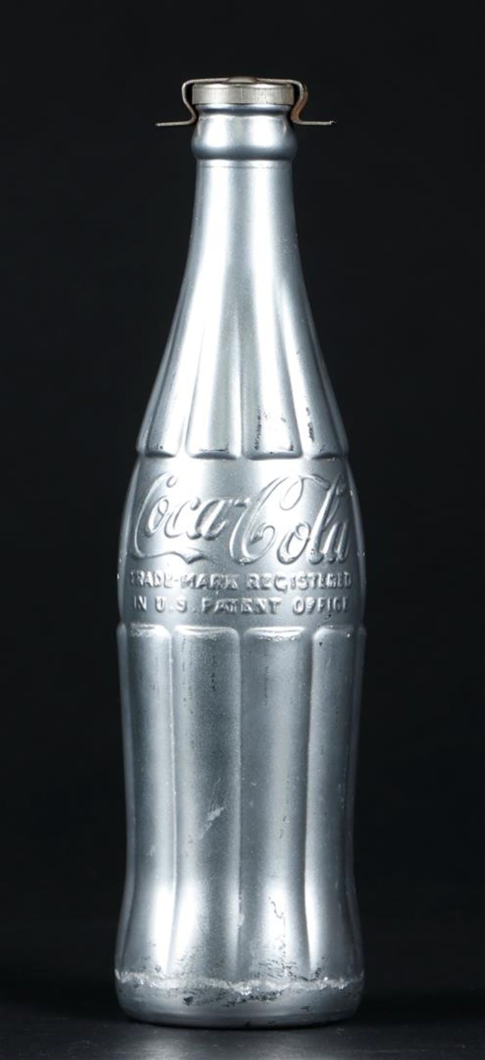 Andy Warhol Pittsburg, Pennsylvania 1928 - 1987 New York) (after), 'You're In': Andy Warhol Pittsburg, Pennsylvania 1928 - 1987 New York) (after), 'You're In' Silver Coca-Cola Bottle with clamp. Carries initials on the clamp, and with label (bottom),25 cm.