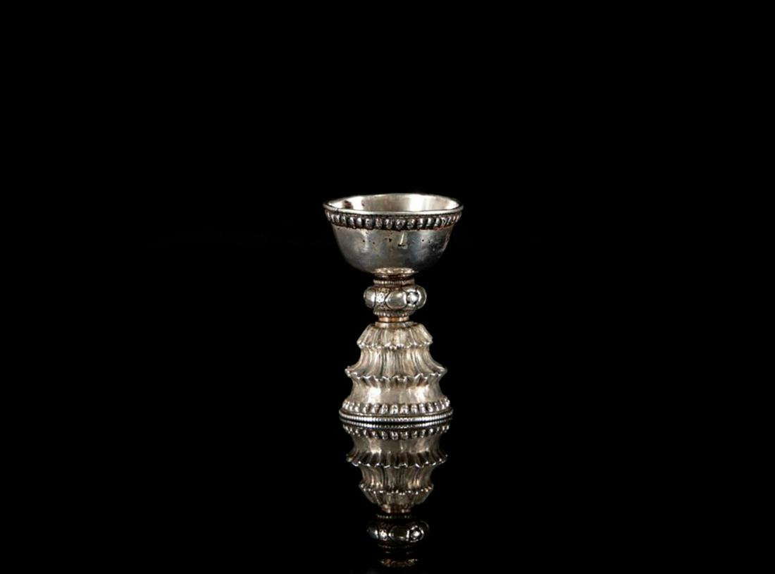 A Tibetan silver butter lamp: A Tibetan silver butter lamp Tibet, 17-18th century. Standing on a floral base, th rim with silver pearls. H. 8,5 cm