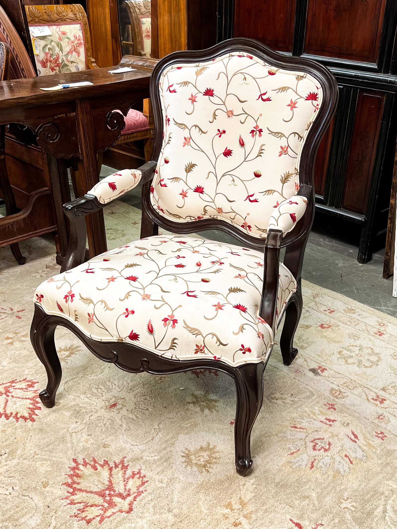 Louis XV Style Floral Upholstered Arm Chair: A Louis XV style arm chair having a scalloped backrest, cabriole legs, floral upholstery on the seat and armrests.