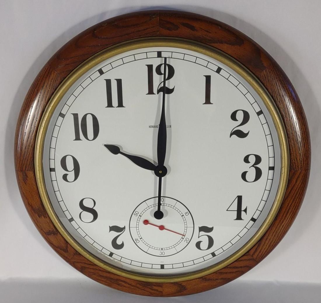 26" Howard Miller Oak Wall Clock 622-757: Made by Howard Miller Clock Company. Battery operated, in working condition. Oak frame. 26" wide. Clock face has stain present between the 6 and 8 mark.