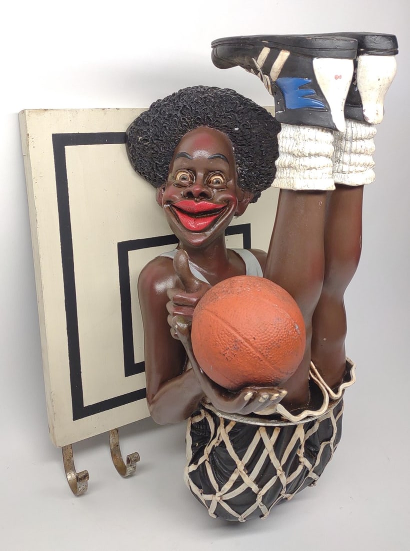 Basketball Player Sculpture by Adelita Bernardo: A cartoon / caricature style sculpture of black basketball player sitting in hoop. Foot is stamped with A.W. Design 2001. Backside has a label Made in the Philippines by Adelita Bernardo. Made of a re