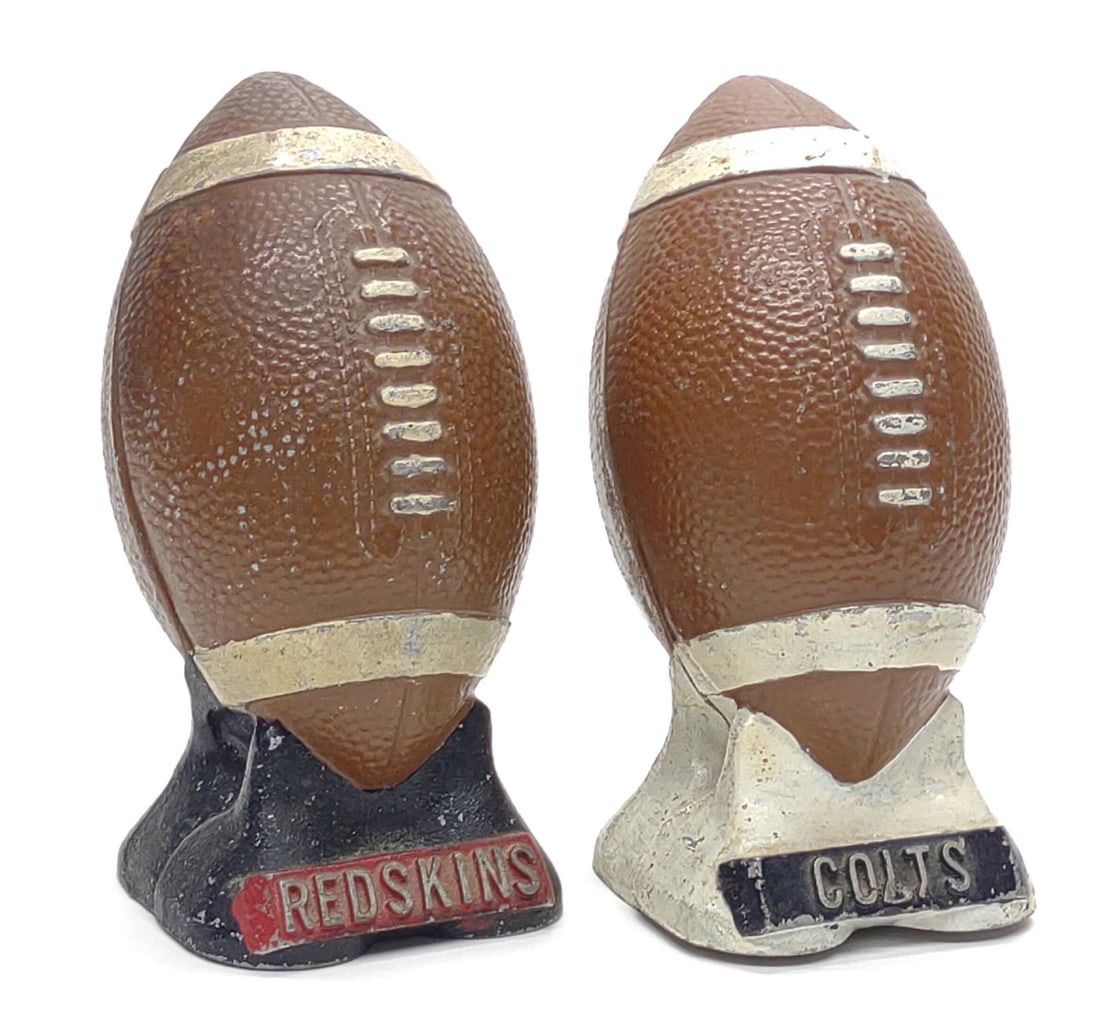 (2) Vintage Redskins & Colts Metal Football Banks: Vintage 1940's Washington Redskins and Baltimore Colts NFL football teams cast aluminum coin still banks produced by First National Bank & Trust. Each bank measures approx. 6 x 3 x 3 in. SHIPPING