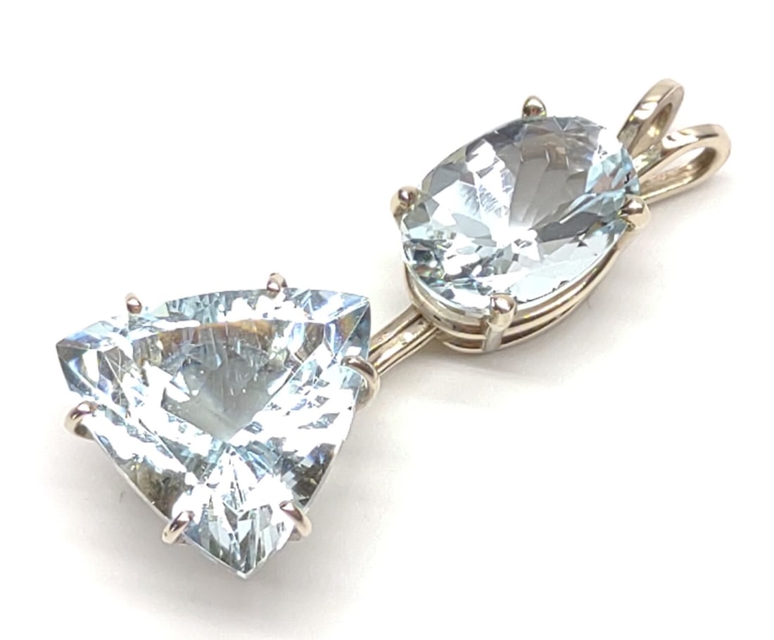 14K W. Gold Aquamarine Trillion & Oval Cut Pendant: 14 karat white gold drop necklace pendant with two large aquamarine stones. Oval cut aquamarine, 14mm x 10mm. Trillion cut aquamarine, 16mm x 16.5mm. Marked "14K" with star symbol. Has been tested for