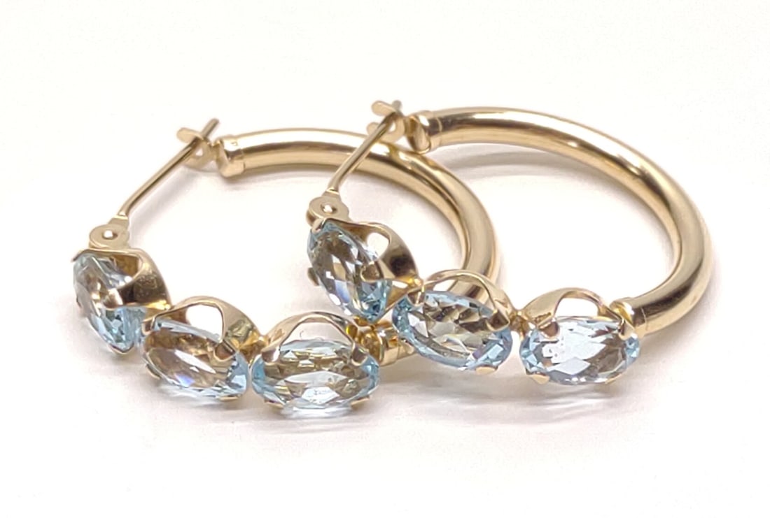 14K Gold & Blue Topaz Hoop Earrings: A pair of 14 karat yellow gold and blue topaz hoop earrings. Features triple mounted oval cut blue topaz 6x4mm (3.42 ctw). RI: 1.62. Marked "S 14K". Has been tested for gold purity and stones. Total w
