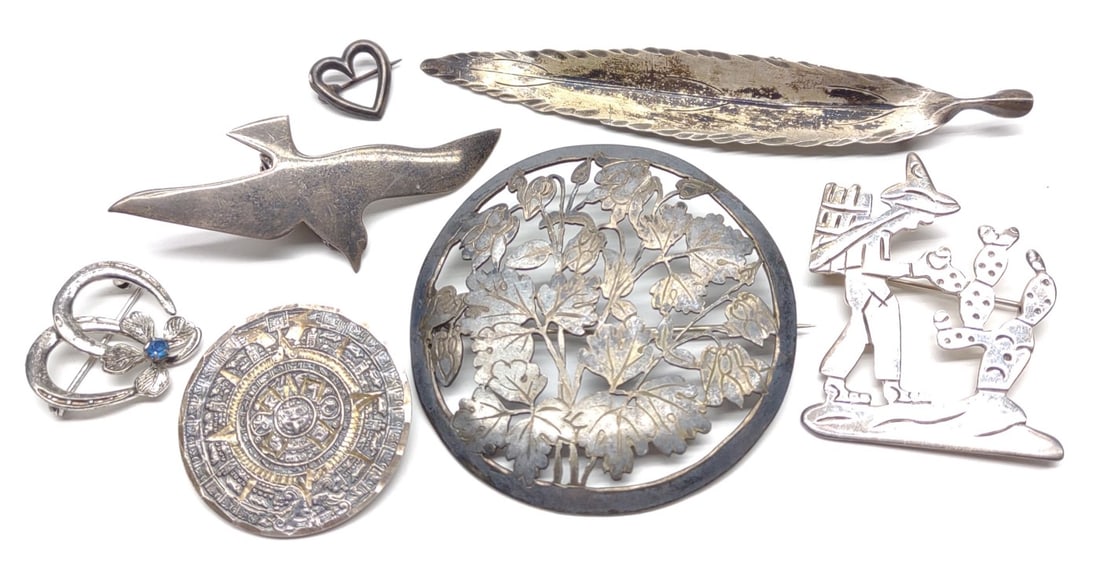 7 Sterling Silver Brooches (Incl. Nye & Taxco): A group of 7 sterling silver figural brooches and pins. Includes Stuart Nye signed feather brooch, International sterling flying bird clip brooch, taxco brooch of man collecting flowers from cactus, a